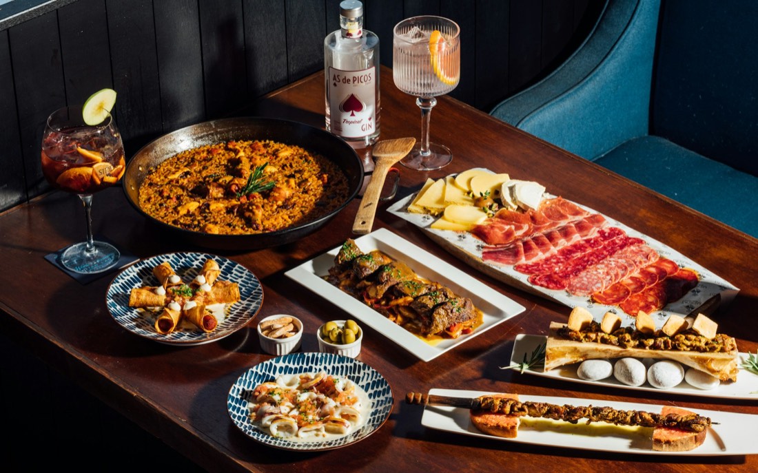 A table laden for sharing: paella, jamón and cured sausage, cheeses, tapas and drinks