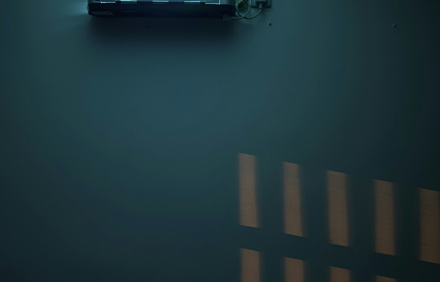 Dark wall with a split unit running up high and the light from the window cast on the wall