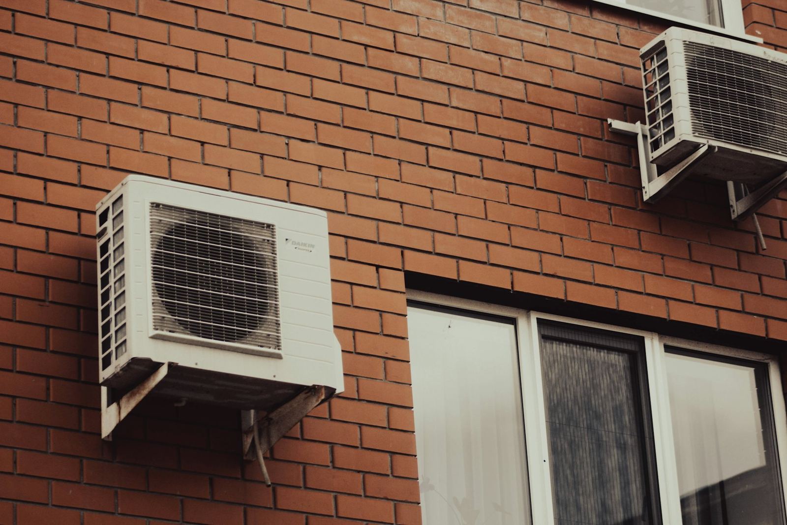 Brick façade of a block of flats with two outdoor units on brackets above a window