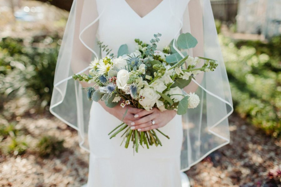 Bride in a veil holding a bouquet of white roses, blue sea holly and eucalyptus