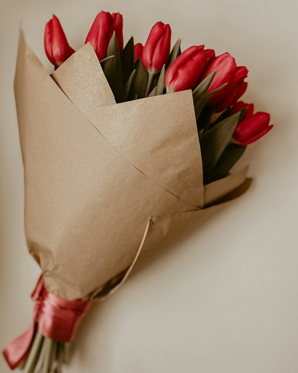 Red tulips wrapped in kraft paper with a red ribbon