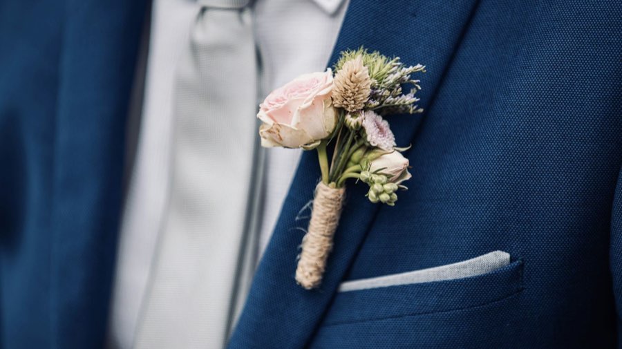 Prendido de rosa rosa y cardo, atado con yute, en la solapa de un traje azul