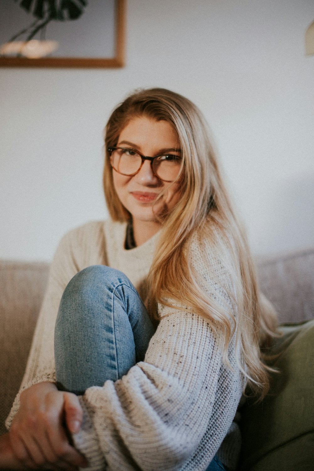 Retrato de muestra: una mujer rubia con gafas, sentada en un sofá y sonriendo