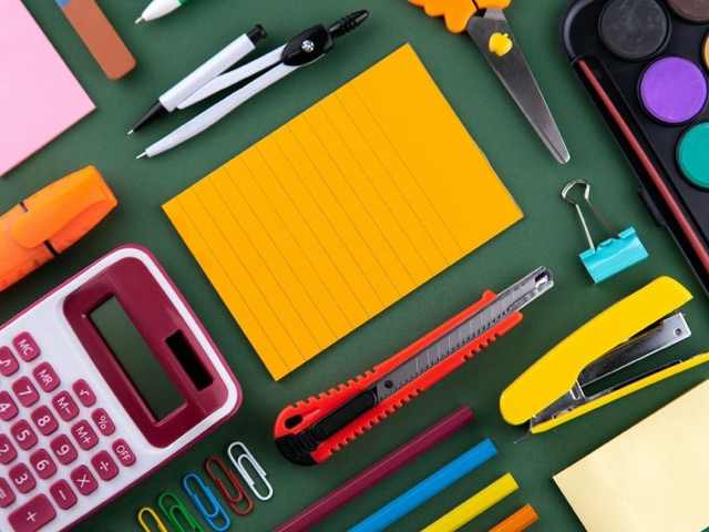 Calculator, compass, scissors, stapler, watercolours and pencils on a green background