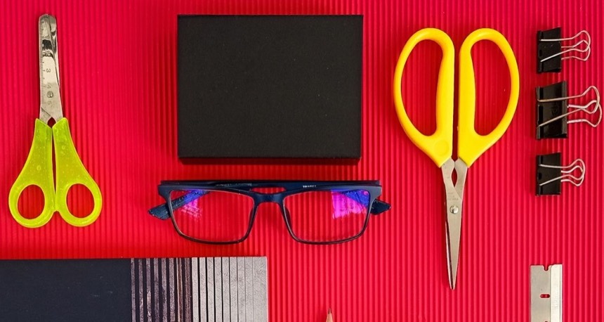 Tijeras, pinzas y unas gafas sobre una cartulina roja