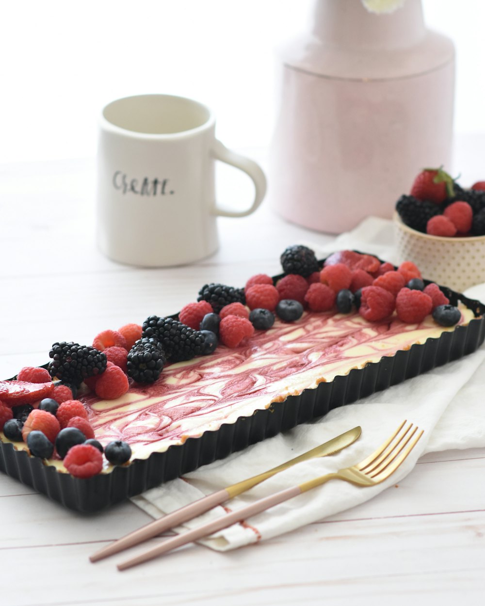 Cheesecake rectangular con frutos rojos y remolinos rosas, en un molde negro