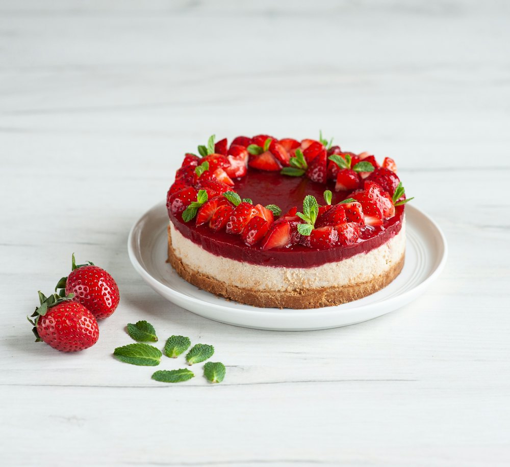 Cheesecake de fresas entero sobre un plato blanco, con fresas y hojas de menta al lado