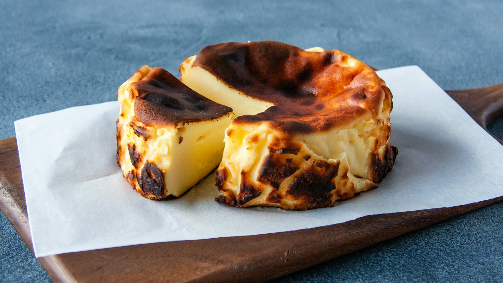 Portada del recetario: tarta de queso vasca partida por la mitad, sobre un papel y una tabla de madera