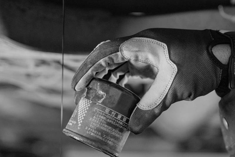 Mano con guante quitando el filtro de aceite mientras cae el aceite viejo